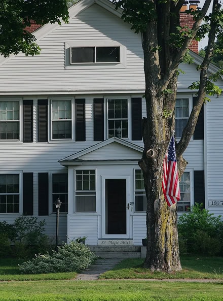 Charming white two-story house with black shutters, an American flag hanging from a tree in the front yard, and "39 Maple Street" on the front step—perfect for your next CT Home Inspection.