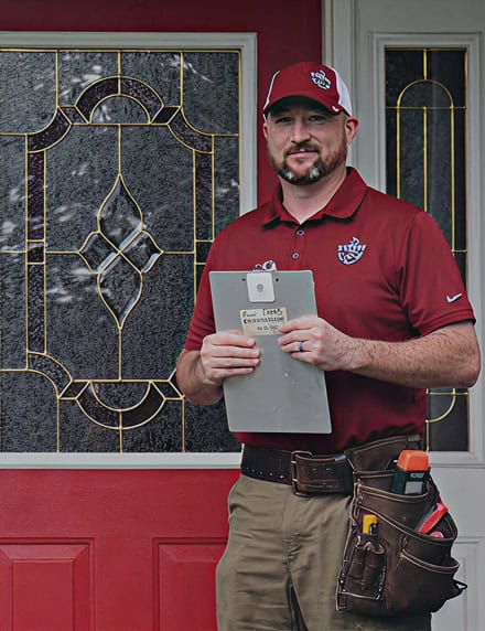 A man in a red polo shirt and cap stands in front of a red door, holding a clipboard and wearing a tool belt—ready for your CT Home Inspection.