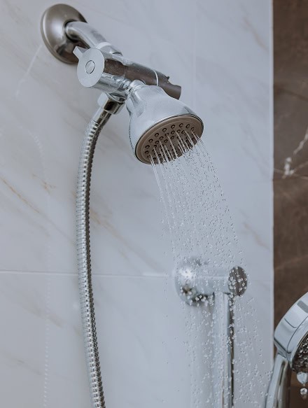 A close-up of a handheld shower head attached to a wall, spraying water in a modern tiled bathroom—an essential feature Anchor Home Inspection reviews during every CT home inspection.