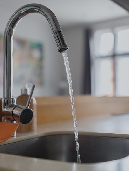 A kitchen faucet with running water, positioned over a stainless steel sink; a soap dispenser is nearby on the countertop, showcasing details often evaluated during a CT Home Inspection.
